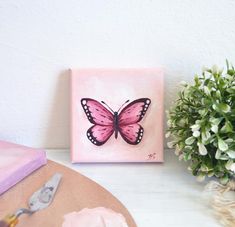 a painting of a pink butterfly sitting on top of a table next to a potted plant