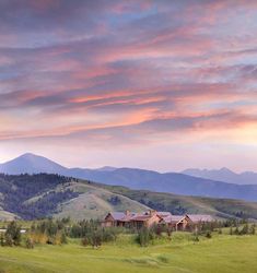 a large house sitting on top of a lush green hillside under a cloudy blue sky