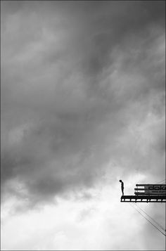 a person standing on top of a wooden bench under a cloudy sky with an airplane in the background