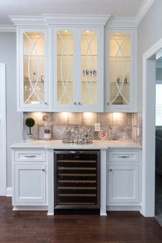 a kitchen with white cabinets and wood flooring is pictured in this image, the wine cellar has glass doors on both sides