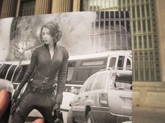 a hand holding up a black and white photo of a woman in front of a building