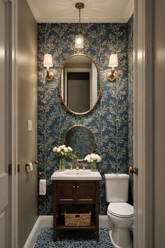 a bathroom with blue and white wallpaper, gold mirror, toilet and sink in it