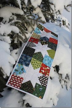 a patchwork quilt hanging from a tree branch in the snow, with lots of snow on it