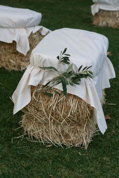 two hay bales with white covers and an olive branch tied to them on the grass