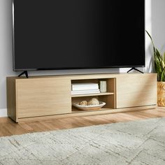 a flat screen tv sitting on top of a wooden entertainment center next to a potted plant