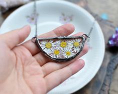 a hand holding a small piece of glass with daisies in it on a plate