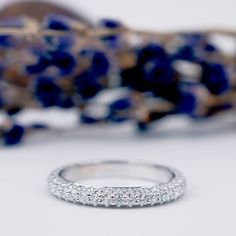 a diamond wedding band sitting on top of a table next to a blue flower arrangement