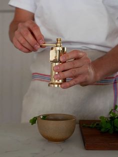 a person in a white shirt is holding a golden object near a bowl and knife