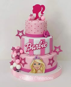 a pink and white cake with barbie doll on it's top, surrounded by stars