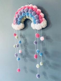 a crocheted rainbow mobile hanging on the wall with pom - poms