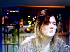 a woman with long hair is talking on the television screen while wearing a striped shirt