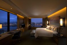 a hotel room with a large window overlooking the city at night, and a king size bed