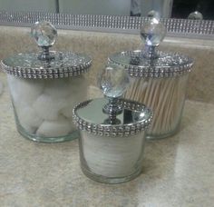 two glass jars with crystal knobs on them sitting on a marble counter top next to a mirror