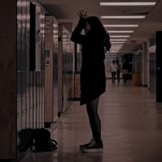 a woman standing in a hallway next to lockers with her hand on her head