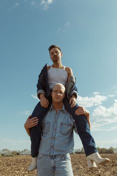 two men are carrying one another on his shoulders in the middle of an open field