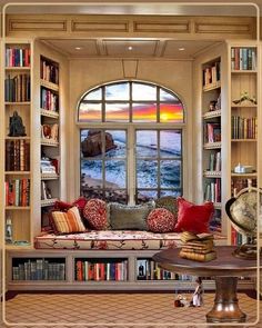 a living room filled with furniture and bookshelves next to a window overlooking the ocean