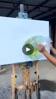 a man is painting on an easel in front of a white board with green and yellow swirls