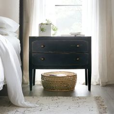 a bed with white sheets and pillows next to a night stand in front of a window