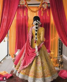 a woman in a yellow and pink lehenga standing under red drapes with flowers on the floor