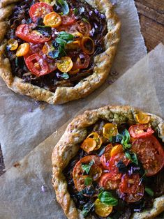 two pies with different toppings sitting on top of wax paper next to each other