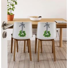 two chairs with christmas wreaths on them sitting in front of a dining room table