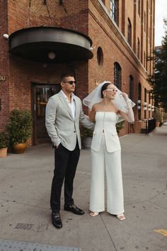 a man and woman standing on the sidewalk in front of a building with a veil over their eyes