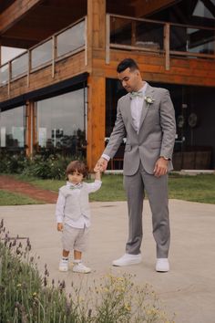 a man holding the hand of a small child in front of a building with flowers