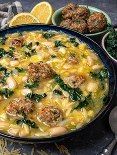 a bowl of soup with meatballs, spinach and lemons on the side