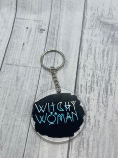 a keychain with the words witch woman written in blue ink on a white wood background