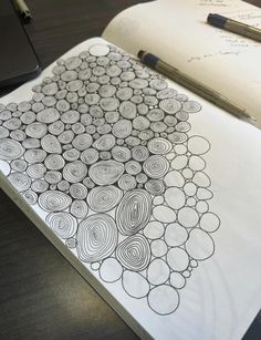 an open notebook with circles drawn on it next to a pen and laptop computer sitting on a desk