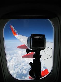 the view from an airplane window looking out at clouds and blue sky with a camera attached to it