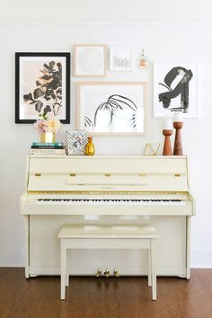 a white piano sitting in the middle of a room with pictures on the wall above it