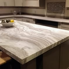 a bowl of fruit on top of a marble countertop in a kitchen with stainless steel appliances