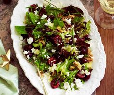 a salad with cherries and goat cheese on a plate next to a glass of wine