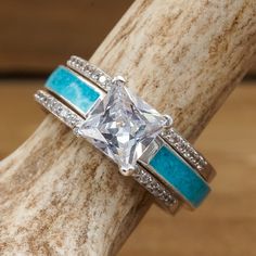 a diamond and turquoise stone ring set on top of a tree branch with wood in the background