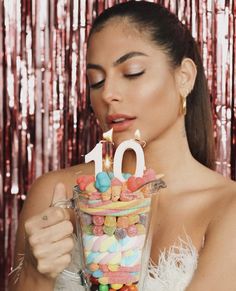 a woman blowing out the candles on her birthday cake that is surrounded by candies