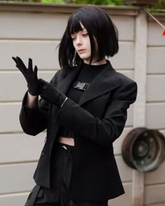 a woman with black hair and bangs standing in front of a garage door wearing a black coat