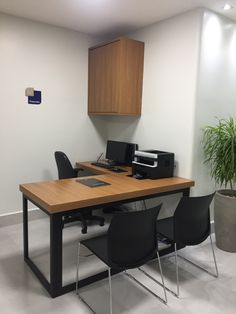 an office desk with computers and printer on it in front of a potted plant