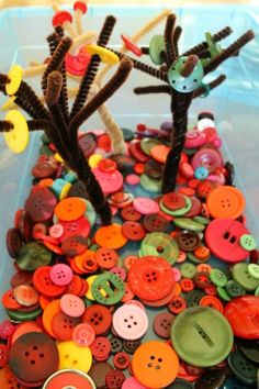 a plastic container filled with lots of different colored buttons and some type of tree on top of it