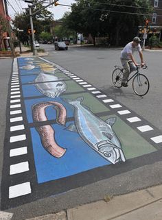 a man riding a bike down a street next to a sidewalk painted with fish and octopus