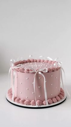 a pink cake with white bows and hearts on it's side, sitting on a plate