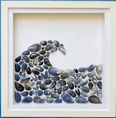 a white frame holding a blue and black art piece with shells in it's shape