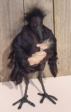 a black bird with long legs holding a stuffed animal in it's beak and standing next to a wooden fence