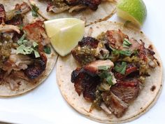 three tacos on a plate with lime and cilantro