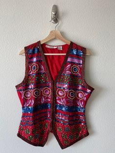 "Fun and funky beaded I. Magnin vest. Features a cute floral design throughout. Hook and eye closures in the front. Vest isn't in perfect condition as there are some snags in some areas, but nothing super noticeable. Most beads are still in tact. Shines so bright day or night. You'll definitely get some attention in this beauty. Can be dressed up or down, it's actually super versatile. Extra attachment of beads pinned inside vest.  Tag reads:  Brand: I. Magnin  100% pure silk  Made in India  Measurements:  Length: 25\"  Pit-to-pit: 20\"  Bust: 38\"" Embellished Bohemian Sleeveless Vest, Red V-neck Vest For Spring, Fitted Bohemian Vest For Festive Occasions, Sequined Fitted Vest For Spring, Fitted Sequin Vest For Spring, Red Vest For Fall Festival, Red Embellished Sleeveless Top, Vintage Red Vest For Summer, Red Vintage Vest For Summer