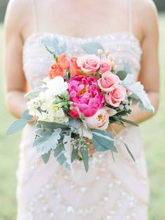 a woman in a dress holding a bouquet of flowers and greenery on her wedding day