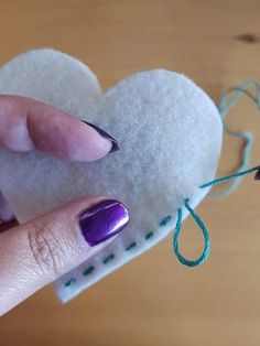 a woman's hand holding a heart shaped piece of felt next to a string