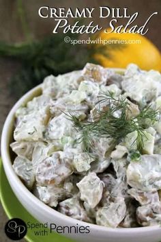 a white bowl filled with potato salad next to lemons and dill on a table