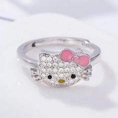 a hello kitty ring with pink bow on the front and black eyes, sitting on top of a white surface