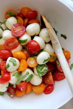 a white bowl filled with mozzarella and cherry tomato salad next to a wooden spoon